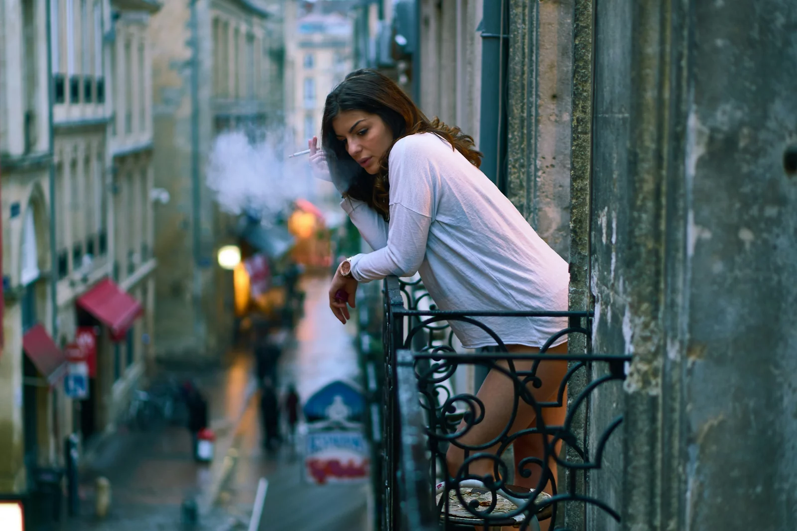 une femme fume une cigarette sur le balcon de sa maison.